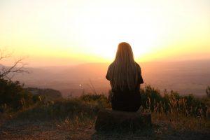 A woman sitting on a rock and looking at the distance. Moving alone will help you have more time for yourself. 